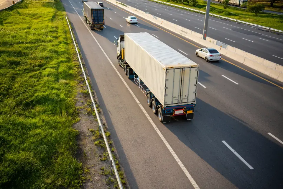 Semi truck with a white container trailer driving on a multi-lane highway beside a grassy shoulder